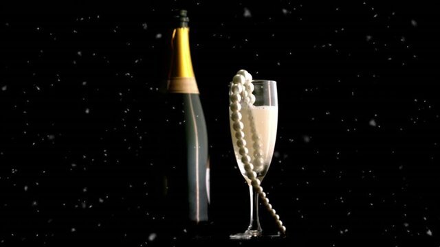 White particles over pearl beads on a champagne glass and champagne bottle on black background