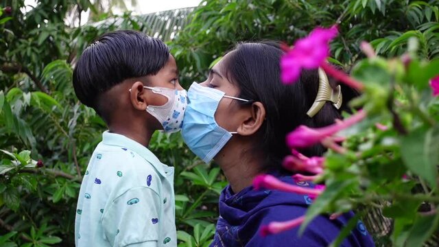 Asian mothers and children are kissing and loving each other while wearing safety masks. Hygiene and safety concept. Mom and the kid have happy moments in the green garden. Slow-motion video. 