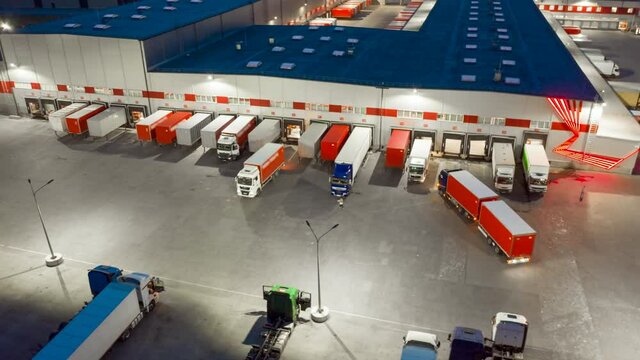 Aerial hyper lapse (hyperlapse - motion time lapse) of a logistics park with a loading hub. Semi-trailer trucks standing at warehouse ramps for loading and unloading goods at night