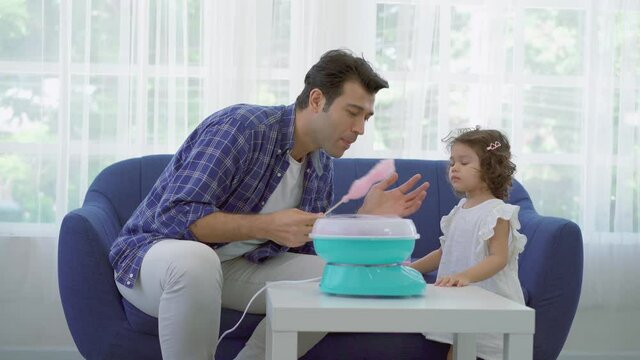 Hand father rolling cotton candy in candy floss machine and eat cotton candy together with daughter on sofa at new house