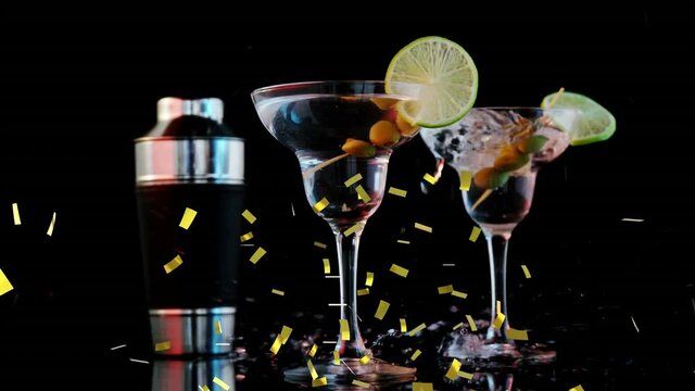 Golden confetti falling over ice cubes falling into cocktail glasses against black background