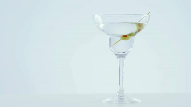 Grey paper burning over olives in cocktail glass against grey background