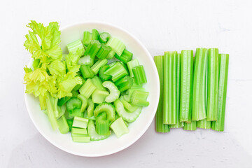 Fresh Chopped Celery Sticks and Slices with Water Drops in White Bowl on White Cutting Board - Top View. Vegan and Vegetarian Culture. Raw Food. Healthy Diet with Negative Calorie Content