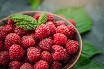 Bowl with fresh ripe delicious raspberries and a green leaves on a black background