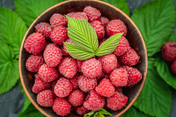 Fresh ripe juicy and appetizing raspberries in a bowl on a black table and green leaves. Top view