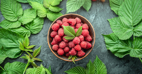 Fresh ripe juicy and appetizing raspberries in a bowl on a black table and green leaves