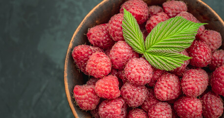 Fresh ripe juicy and appetizing raspberries in a bowl on a black table and green leaves. Top view