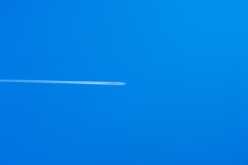 A plane is flying in a clear blue sky leaving a trail behind it