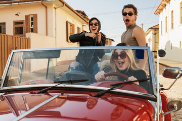 Friends traveling together in an old convertible car. Summer enjoyment concept - obrazy, fototapety, plakaty