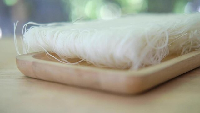 Raw of rice noodles on a wood tray. Panning shot