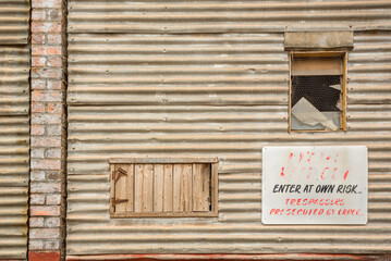 Obraz na płótnie Canvas Old abandoned warehouse wall with weathered timber hatch and faded sign - ‘Enter at own risk’