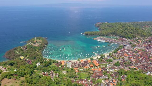 Aerial drone footage of the stunning Padang Bai village beach and harbor in eastern Bali, Indonesia. Shot with a light titl down motion