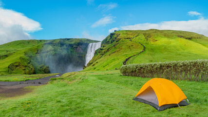 Panoramic view over camping site with orange tent, and tourists in front of famous Skogafoss...