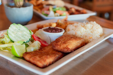Breaded chicken with salad on wooden table with COPY SPACE, Close up of chicken fillet with salad, rice and beans
