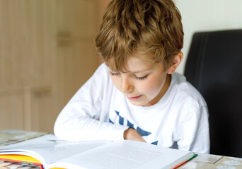 Little blonde school kid boy reading a book at home. Child interested in reading magazine for kids. Leisure for kids, building skills and education concept