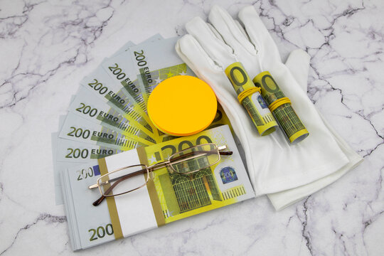Financial or business concept with a pair of white gloves, eyeglasses and wads and fanned 200 Euro banknotes with colorful circular memo pads over a white marble background in a flat lay view