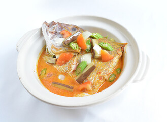 local spicy chilli curry soup big grouper fish head with vegetables in hot clay pot in white background asian halal seafood menu