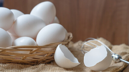 Close-up of white eggs in a bamboo basket, egg shells, and a whisk