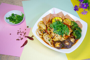 Top view of a delicious hot pot with mushrooms, pork, ham, lotus root, broccoli, and coriander