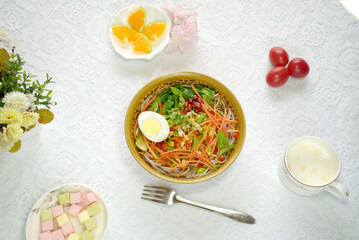 Top view of vegetable rice noodle soup made of eggs, peanuts, and carrot shreds, with cherry tomatoes and oranges on the side
