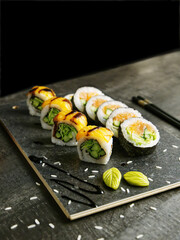 Sushi on a black board with salmon, vegetables, and cucumbers, black background