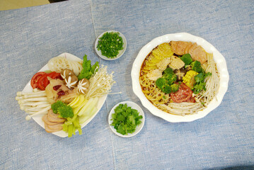 Hot pot ingredients, chopped green onion and celery leaves on a blue background, top view