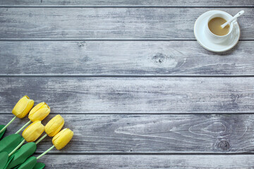 Fototapeta na wymiar A cup of coffee and yellow tulips on a wooden textured table, copy space