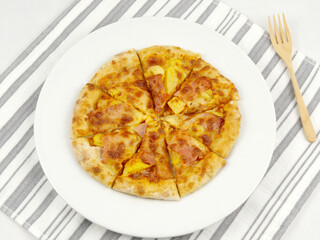 Top view of homemade pizza on a white plate and a fork on a gray and white striped napkin