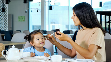 Little daughter helps mom apply make-up, closeup