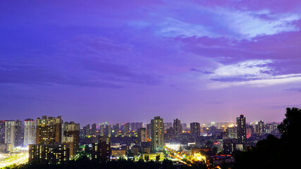 Fototapeta na wymiar The bustling city is brightly lit, with purple night sky. Panoramic view