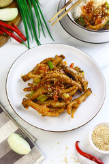 Korean Spicy Chicken feet or ceker ayam saus Gochujang served on white plate with sesame seed and slices onion spring. Bright mood food photography.