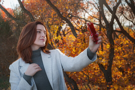 Portrait of a cheerful young woman with autumn leaves in front of the leaves taking selfies