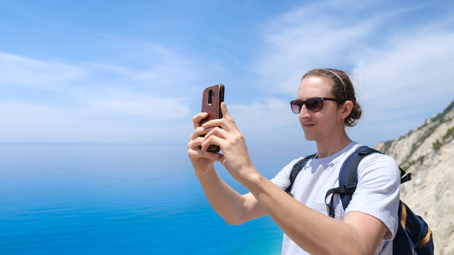 Travel blogger taking pictures of beautiful beach with smartphone. Summertime holidays in Greece concept. Selective focus