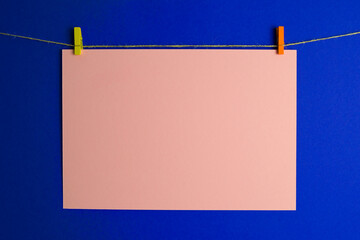 beige sheet of paper suspended from a rope on a blue background. the cardboard is held on a yellow...