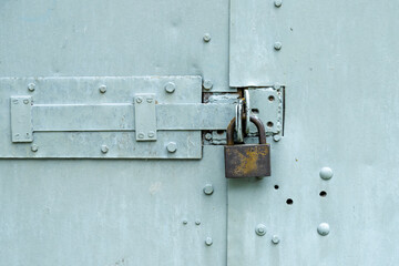Rusty padlock on grey painted metal door or gate with screws