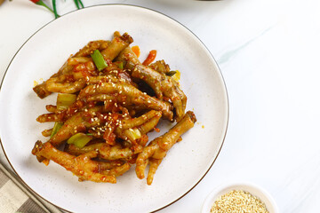 Korean Spicy Chicken feet or ceker ayam saus Gochujang served on white plate with sesame seed and slices onion spring. Bright mood food photography.