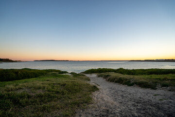 sandy path leading down to the ocean with an orange sunset over the ocean