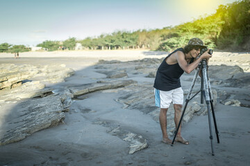 young man taking photo on the beach, man photographing with tripod at sea