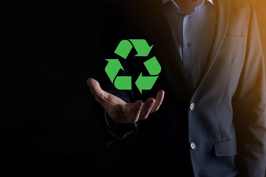 Businessman in suit over dark background holds an recycling icon, sign in his hands. Ecology, environment and conservation concept. Neon red blue light