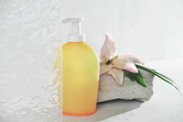 Fototapeta na wymiar yellow unbranded bottle of cosmetic product in bathroom with water drops. floral fragranced shower gel or shampoo in a bottle with pump. self care routine and hygiene