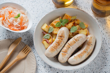 Fried german white sausages with potato salad, sauerkraut and beer, elevated view on a beige granite background