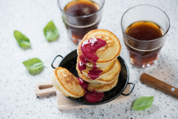 Serving pan with mini pancakes and glasses of black coffee, studio shot on a beige granite background