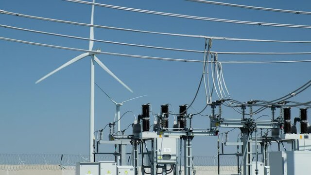 Windmachine generates electricity and power transmission lines of high voltage substation on foreground against blue sky in summer
