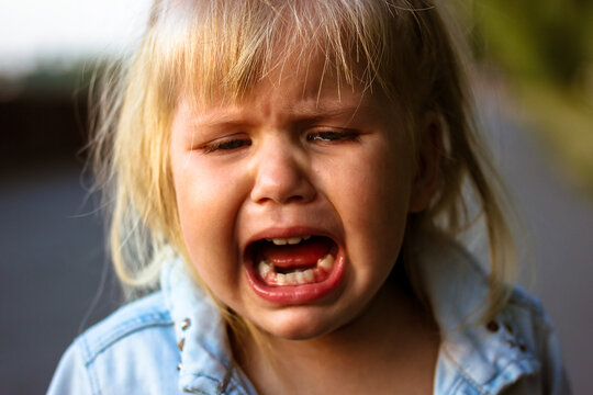 Little cute blonde infant girl is crying outdoors. Upset kid. Child psychology.