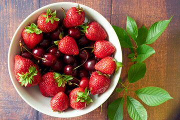 Strawberries and cherries in a white bowl on a wooden table.