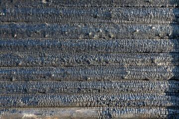 Black burnt wall of a rustic log house on a bright summer sunny day. Coals. Textured surface. Close-up