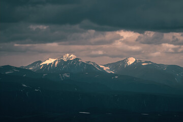 Fototapeta premium Wonderful dramatic landscape with big snowy mountain peaks above low clouds. Atmospheric large snow mountain tops in cloudy sky.