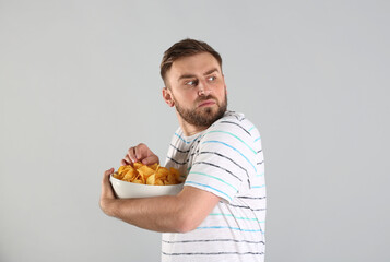 Greedy young man hiding bowl with chips on light grey background - obrazy, fototapety, plakaty