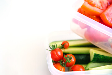 Sliced vegetables in plastic containers on a white background. Cucumbers and tomatoes are in containers.