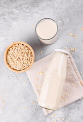 Obraz na płótnie Canvas Vegan non dairy alternative milk. Oat milk in a mug, in a bottle and a bowl with oat flake on grey stone table, above, top view